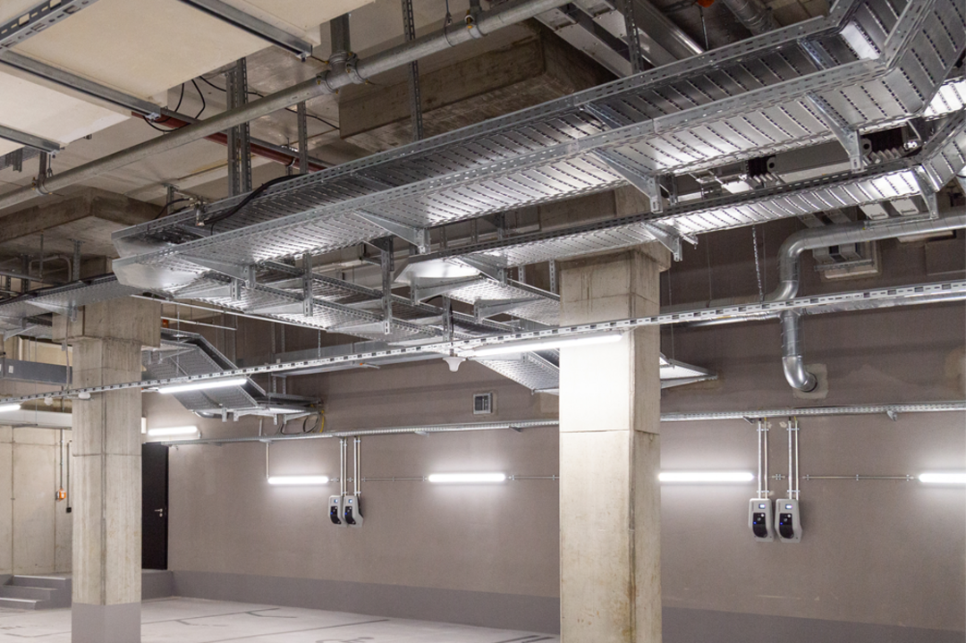 Tiefgarage mit Kabeltragsystemen an der Decke, Betonstützen und mehreren Wallboxen für Elektrofahrzeuge an der Wand.