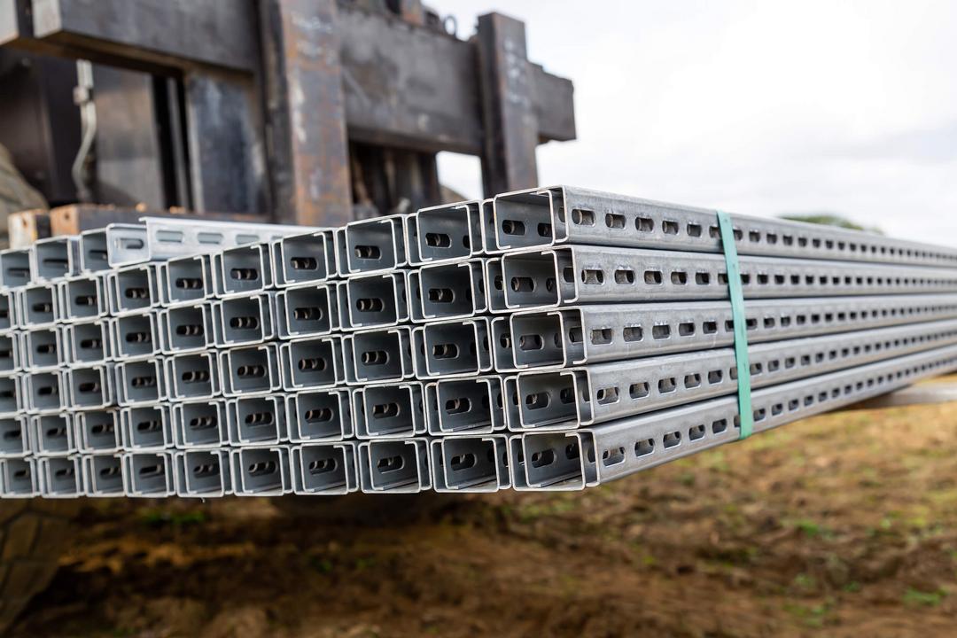 Bündel verzinkter, gelochter Montageschienen liegen gestapelt auf einer Gabel eines Staplers bereit für den Transport zur Baustelle.