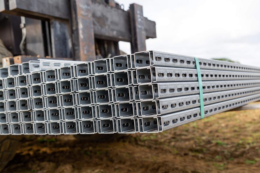 Bündel verzinkter, gelochter Montageschienen liegen gestapelt auf einer Gabel eines Staplers bereit für den Transport zur Baustelle.