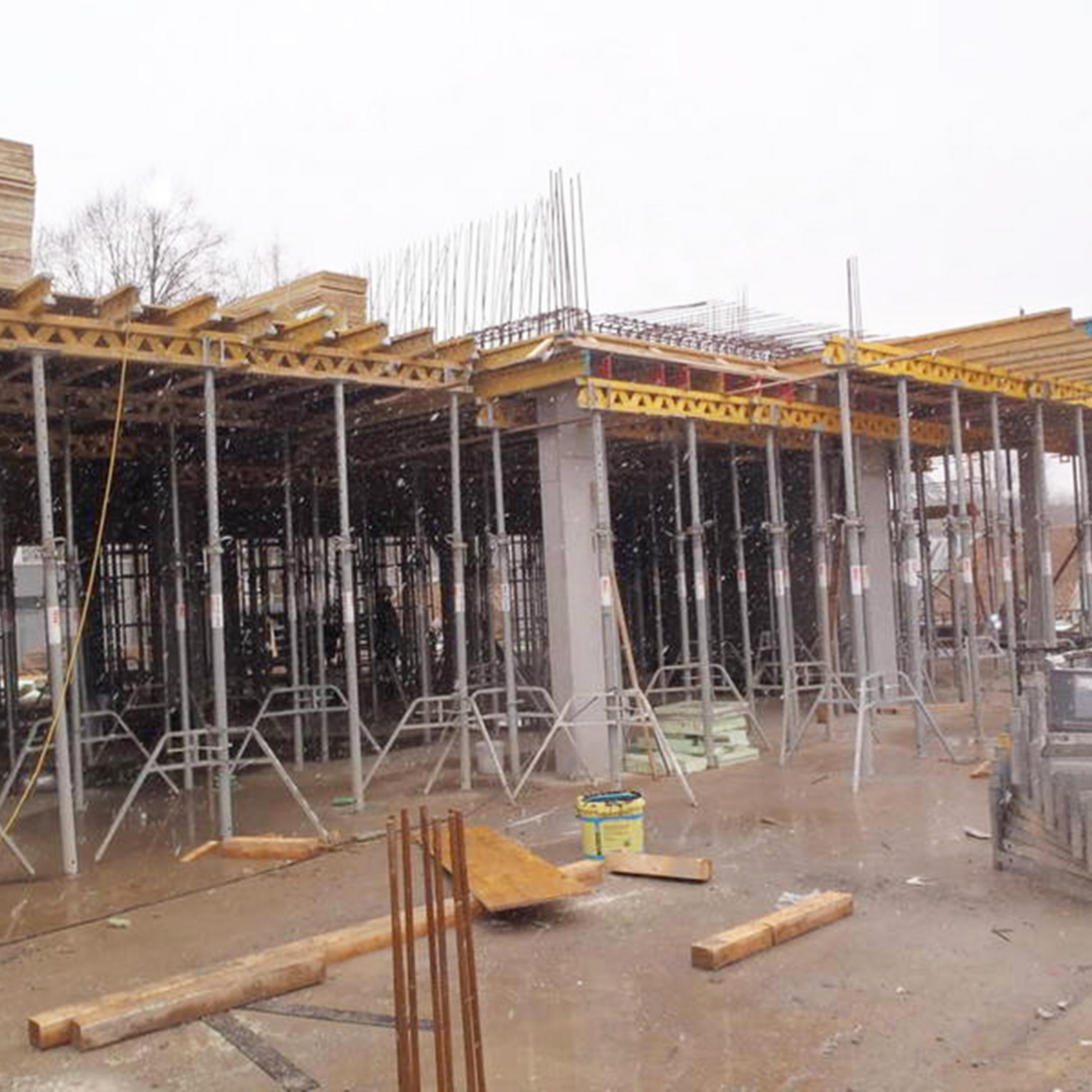 Baustelle mit Gerüsten, Holzplanken, Betonpfeilern und leichtem Schneefall, Materialien liegen verstreut