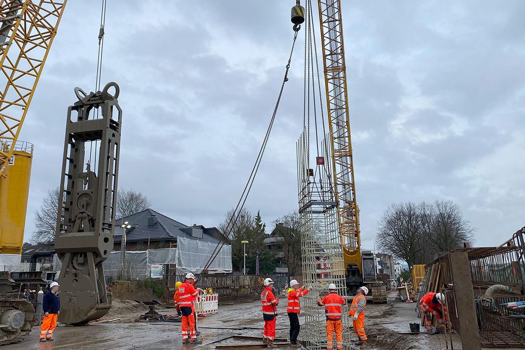 Bauarbeiter überwachen den Einsatz eines Krans beim Heben eines Bewehrungskorbs auf einer Baustelle an einem bewölkten Tag