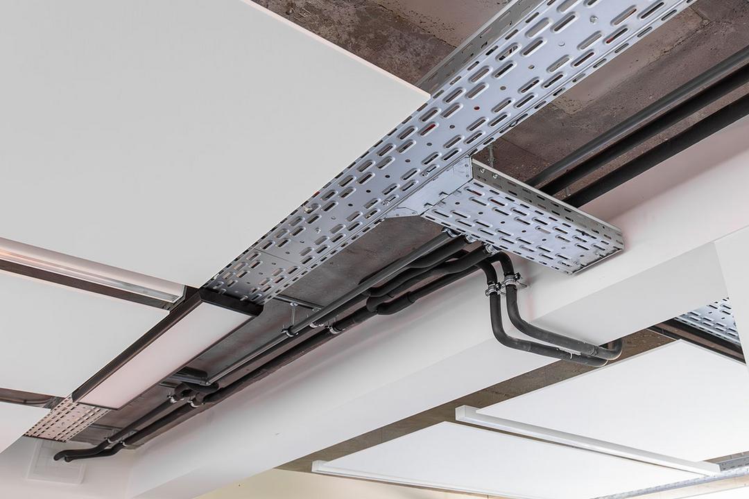 Eine von der Decke hängende, nicht lackierte Kabelrinne für Deckenlampen, aus etwas größerer Entfernung fotografiert.