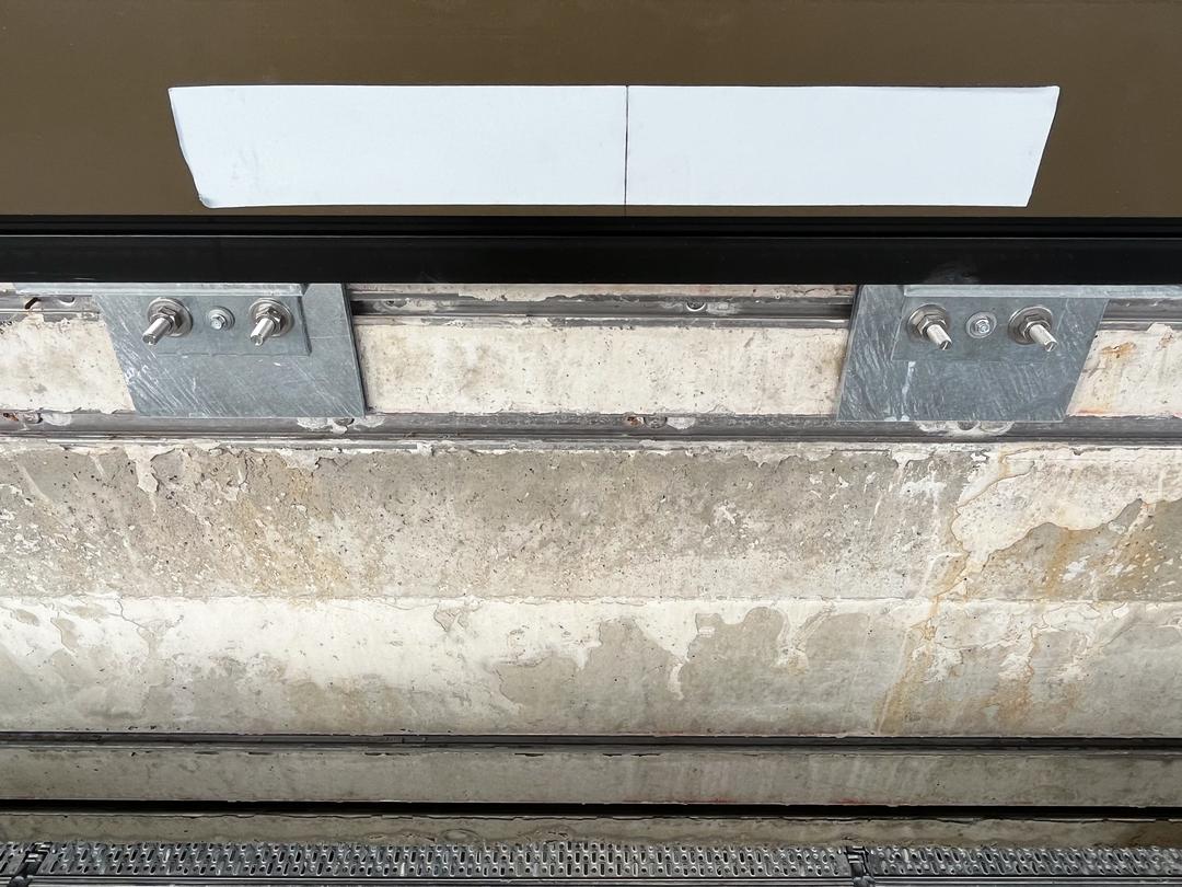 Metallhalterung mit Schrauben an Betonwand, darüber braunes Bauelement mit Klebestreifen.
