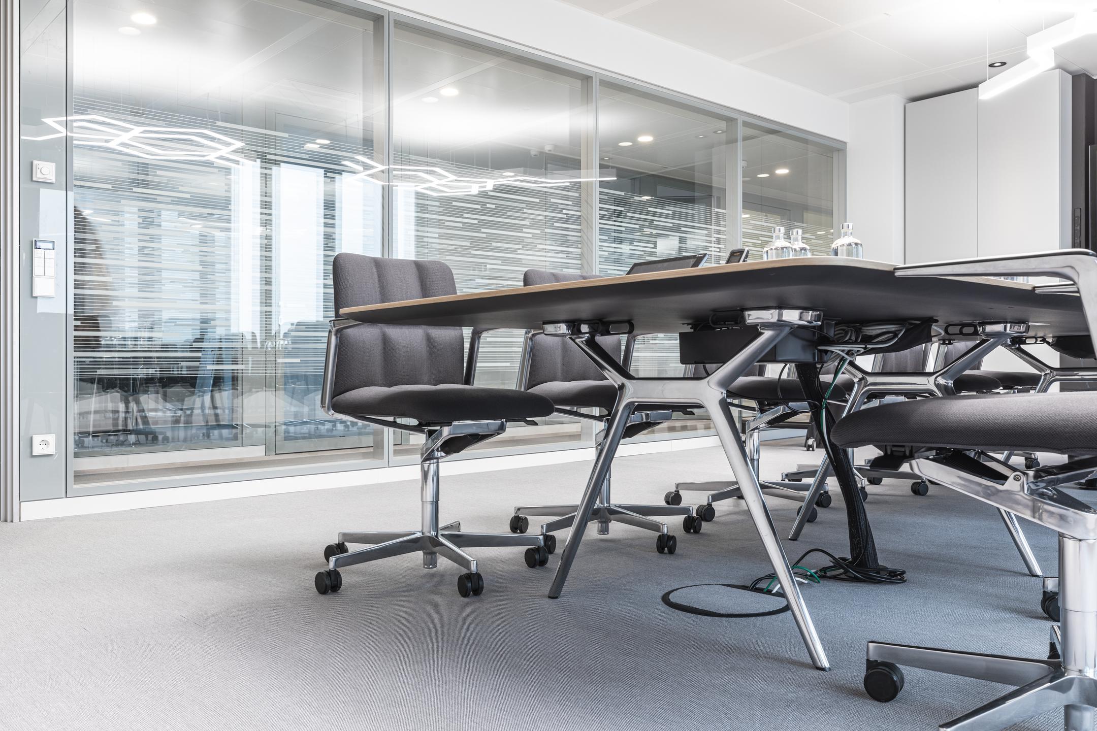 Ein helles Büro mit einer Glaswand im Hintergrund und Tisch und Stühlen im Vordergrund.