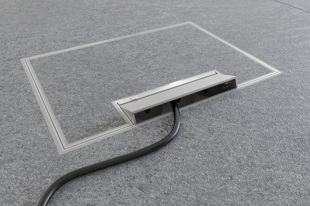 Bodenkanal mit rechteckiger Bodendose im dunklen Fliesenboden, geöffnet mit herausgeführtem Kabel für Strom- und Datenanschlüsse.