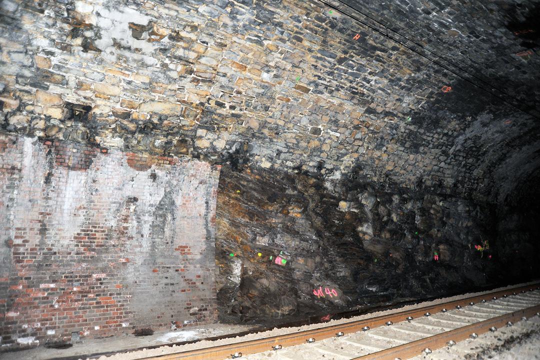 Tunnel mit unregelmäßiger Stein- und Ziegelwand, Eisenbahnschienen, Markierungen auf Felsen, schummerige Beleuchtung