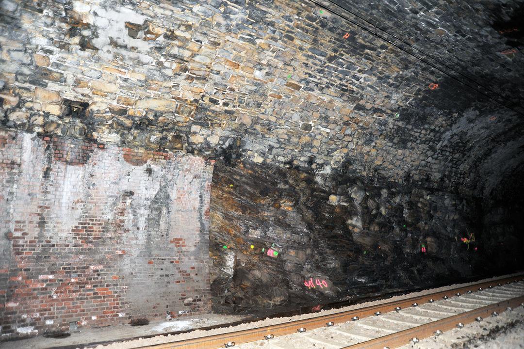 Tunnel mit unregelmäßiger Stein- und Ziegelwand, Eisenbahnschienen, Markierungen auf Felsen, schummerige Beleuchtung