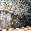 Tunnel mit unregelmäßiger Stein- und Ziegelwand, Eisenbahnschienen, Markierungen auf Felsen, schummerige Beleuchtung