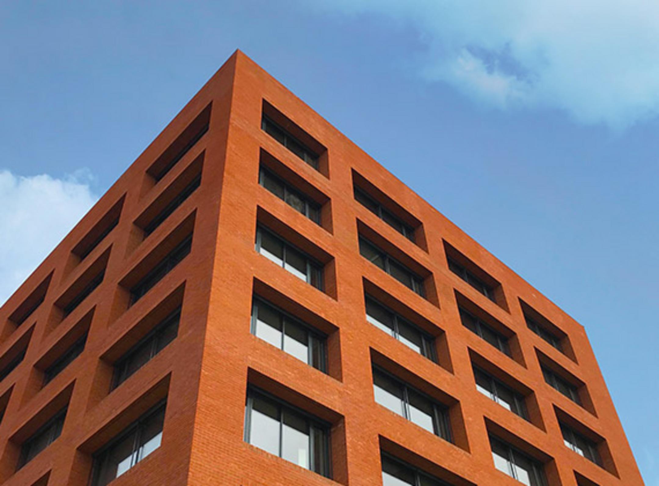 Blick auf ein rotes Backsteingebäude mit vielen Fenstern vor einem blauem Himmel aus der Froschperspektive