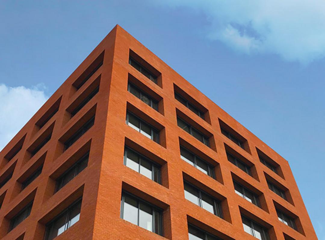 Blick auf ein rotes Backsteingebäude mit vielen Fenstern vor einem blauem Himmel aus der Froschperspektive