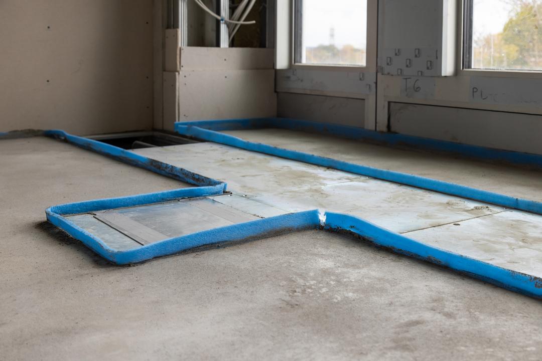 Bodenkanalsystem im Estrichboden, umringt von blauer Schaumstofffolie, im Anschnitt sieht man 2 Fenster