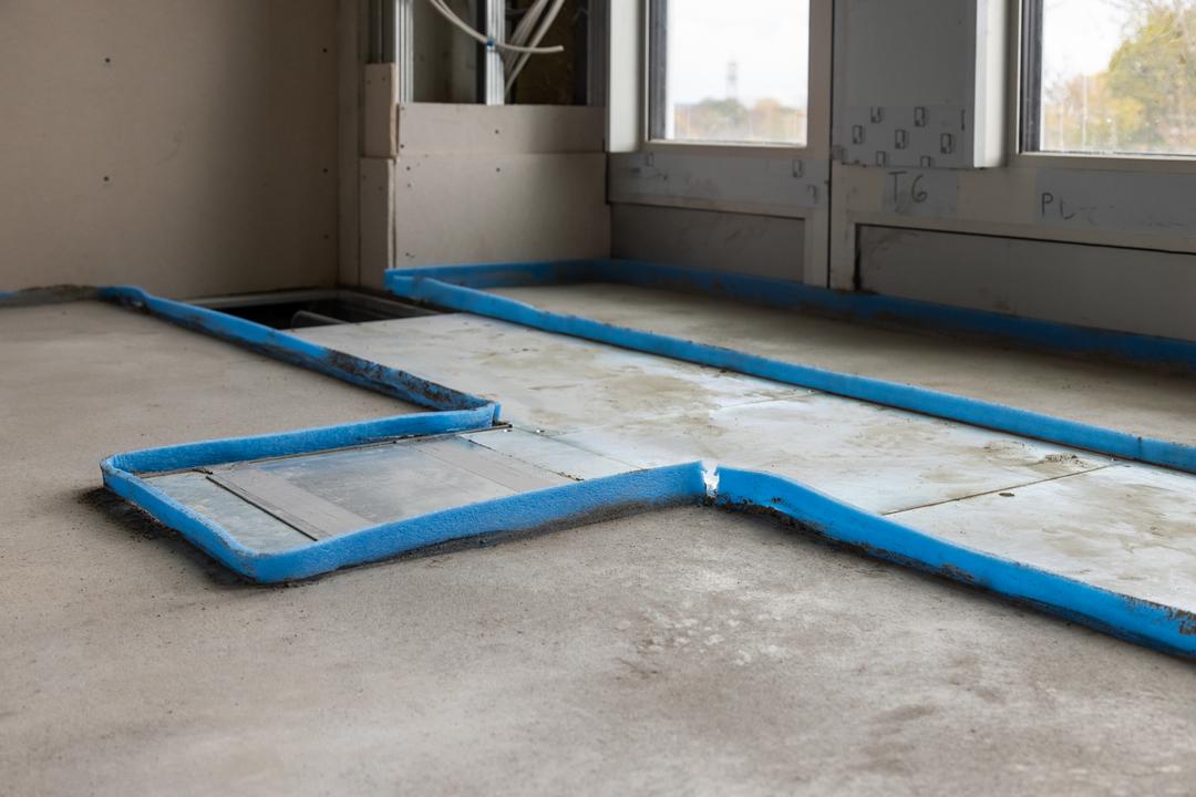 Bodenkanalsystem im Estrichboden, umringt von blauer Schaumstofffolie, im Anschnitt sieht man 2 Fenster