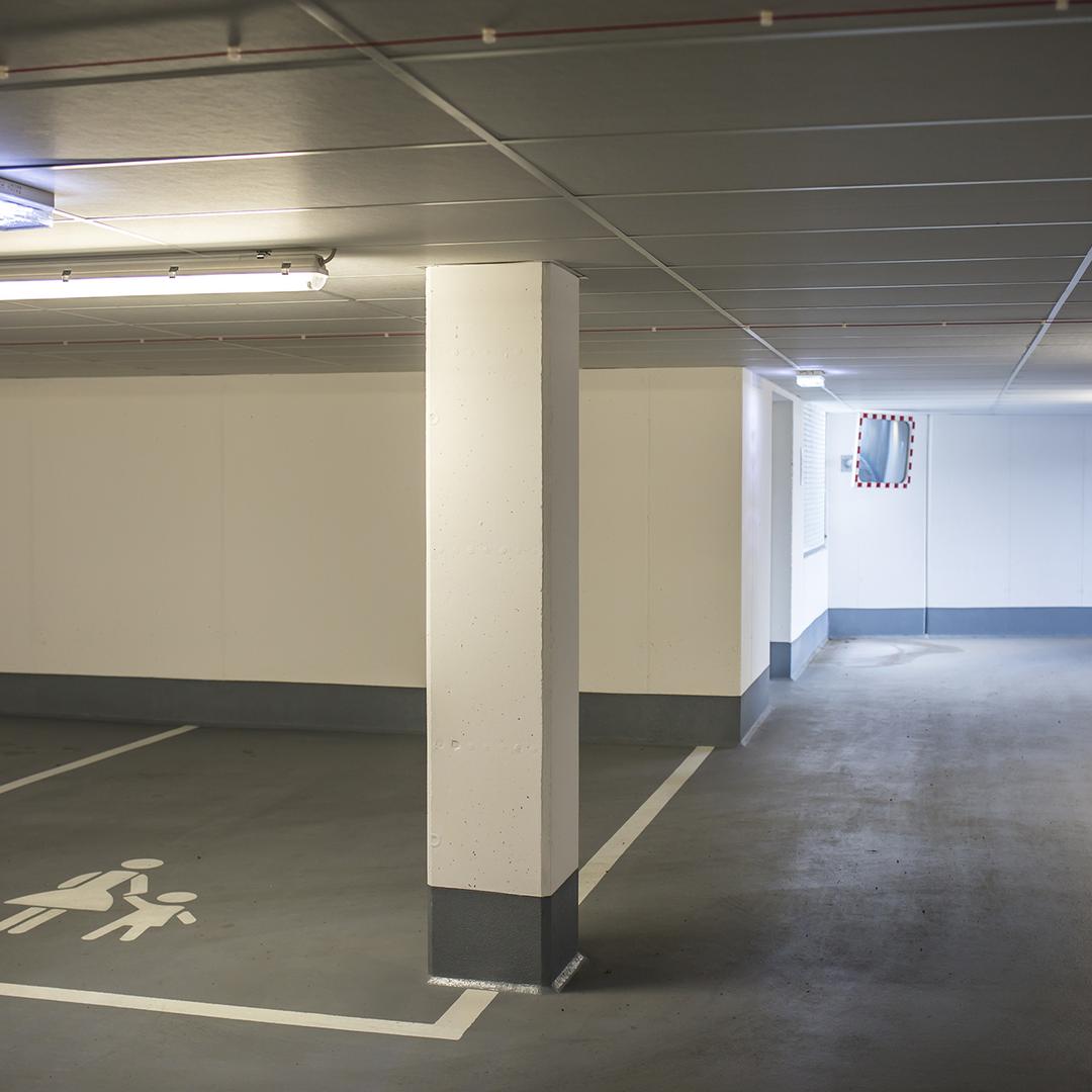 Parkhaus mit Betonpfeiler, markiertem Stellplatz für Eltern mit Kind und einem Spiegel an der Wand zur besseren Übersicht.