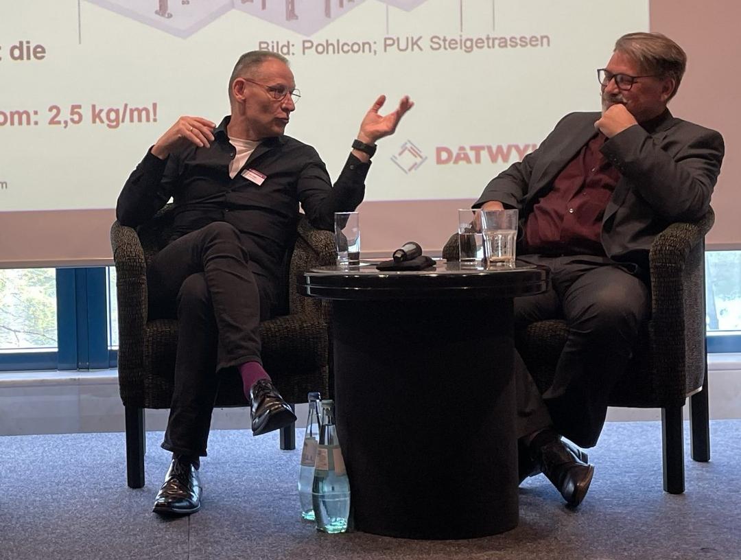 Zwei Männer sitzen bei den Brandschutztagen auf einer Bühne und unterhalten sich gestikulierend.