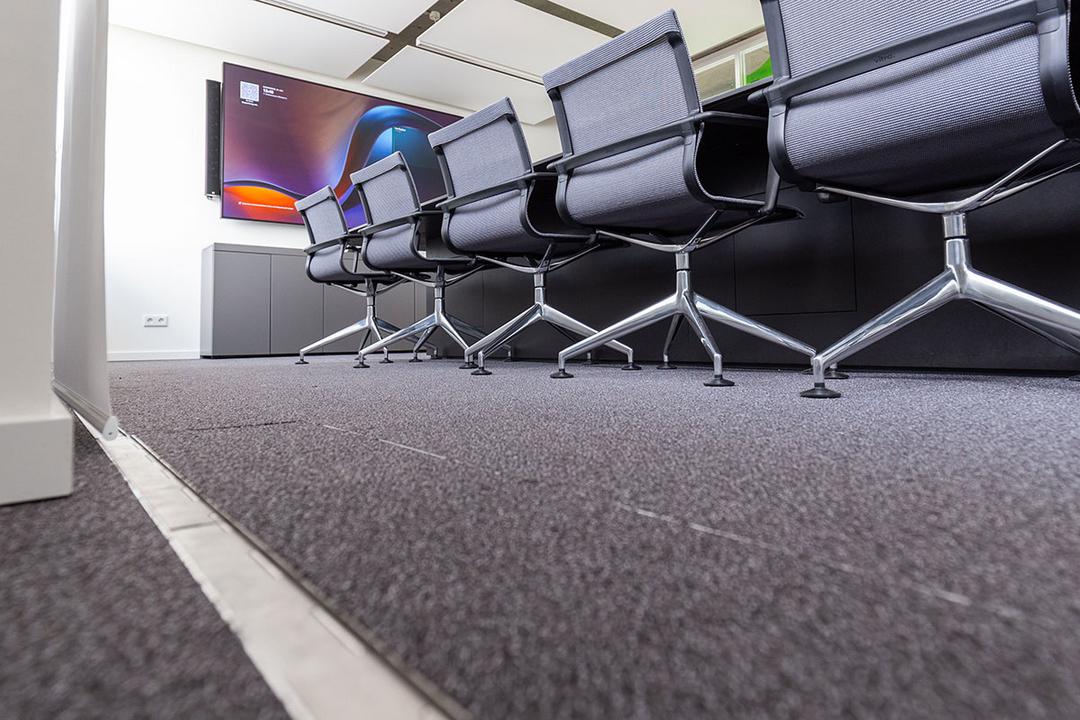 Bürostühle an einem Besprechungstisch von unten, vom in den Boden eingelassenen, geschlossenen Kabelsystem aus fotografiert.