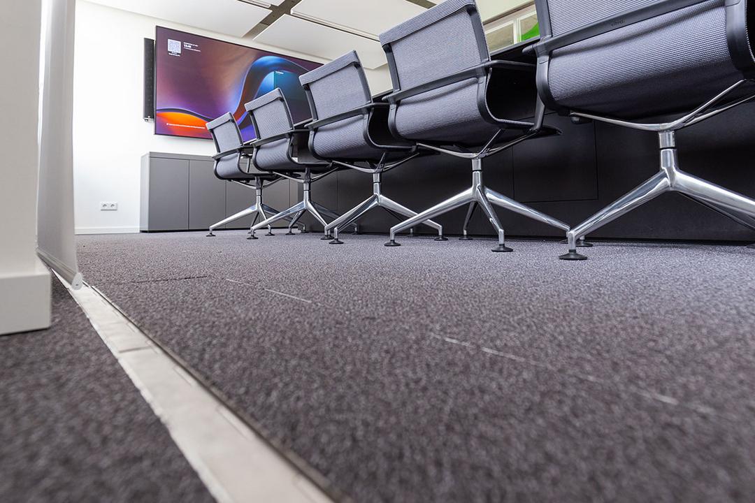 Bürostühle an einem Besprechungstisch von unten, vom in den Boden eingelassenen, geschlossenen Kabelsystem aus fotografiert.