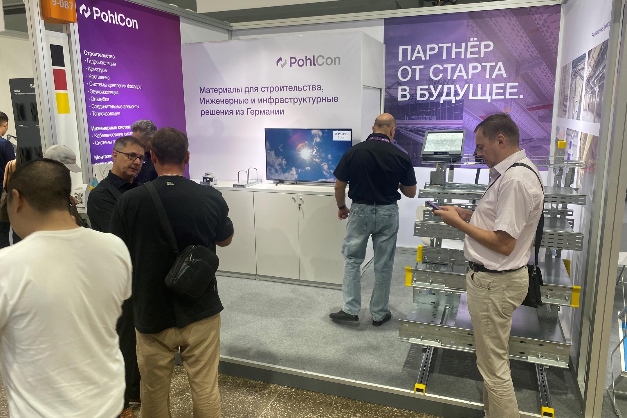 Messestand mit Infotafeln und Besuchern und Modell mit Kabeltragsystemen