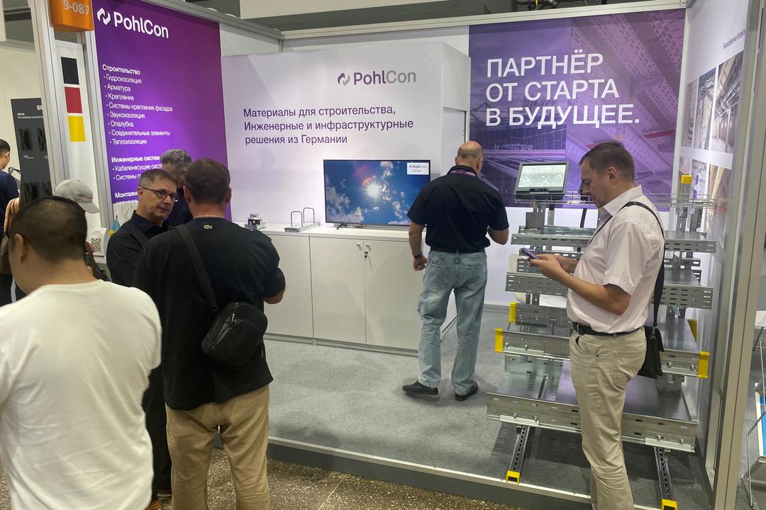 Messestand mit Infotafeln und Besuchern und Modell mit Kabeltragsystemen