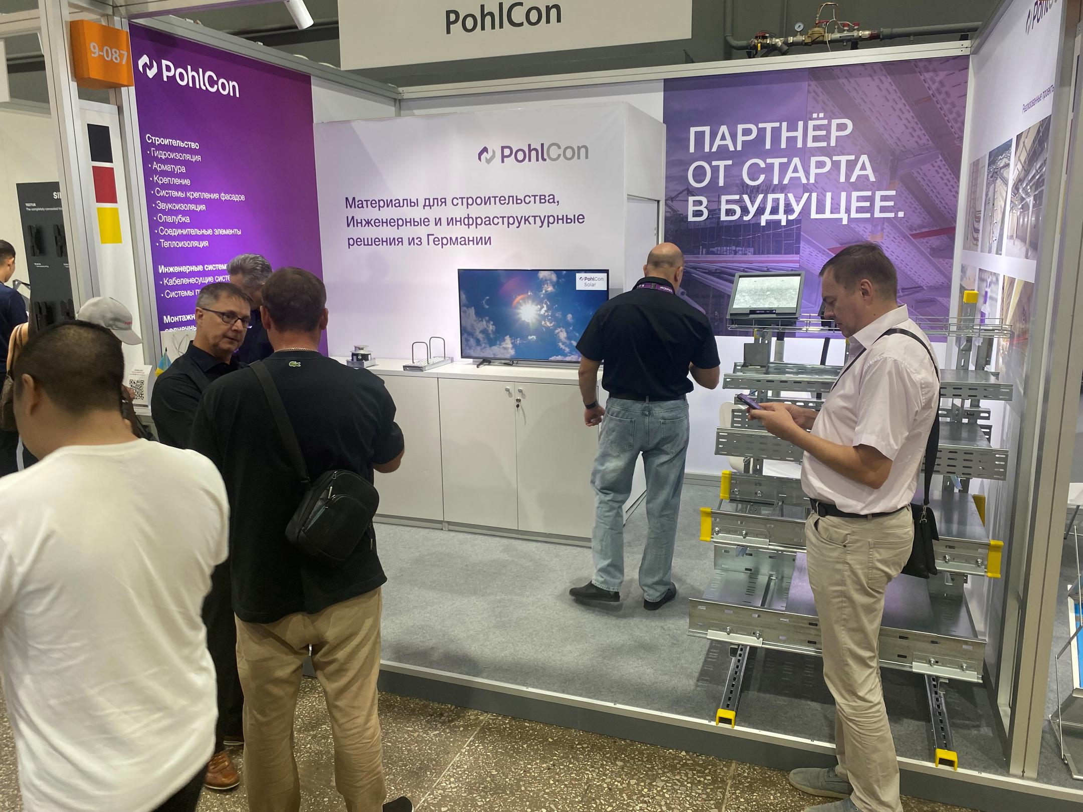 Messestand mit Infotafeln und Besuchern und Modell mit Kabeltragsystemen
