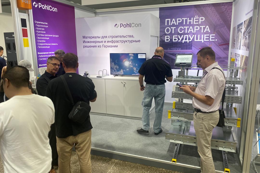 Messestand mit Infotafeln und Besuchern und Modell mit Kabeltragsystemen