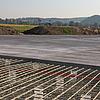Blick auf die Baustelle aus einer anderen Perspektive, auch hier im Hintergrund grüne Felder und Wälder sowie blauer Himmel.