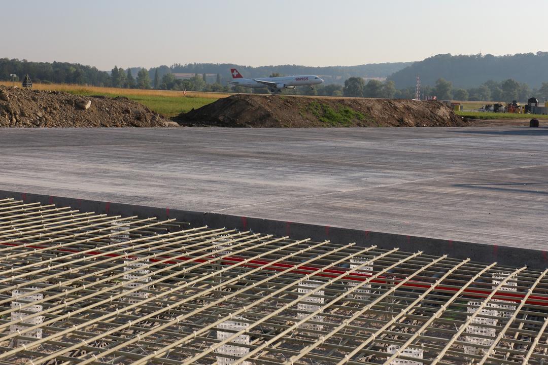 Blick auf die Baustelle aus einer anderen Perspektive, auch hier im Hintergrund grüne Felder und Wälder sowie blauer Himmel.