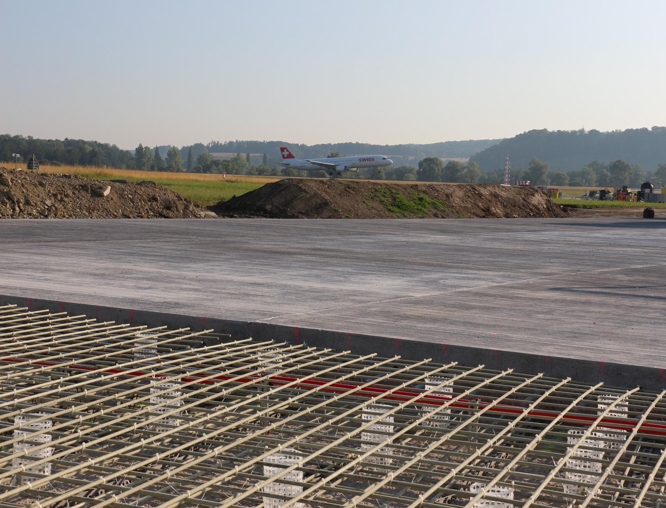 Blick auf die Baustelle aus einer anderen Perspektive, auch hier im Hintergrund grüne Felder und Wälder sowie blauer Himmel.