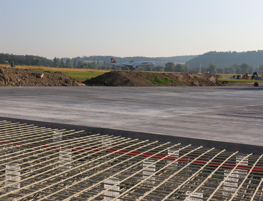 Blick auf die Baustelle aus einer anderen Perspektive, auch hier im Hintergrund grüne Felder und Wälder sowie blauer Himmel.