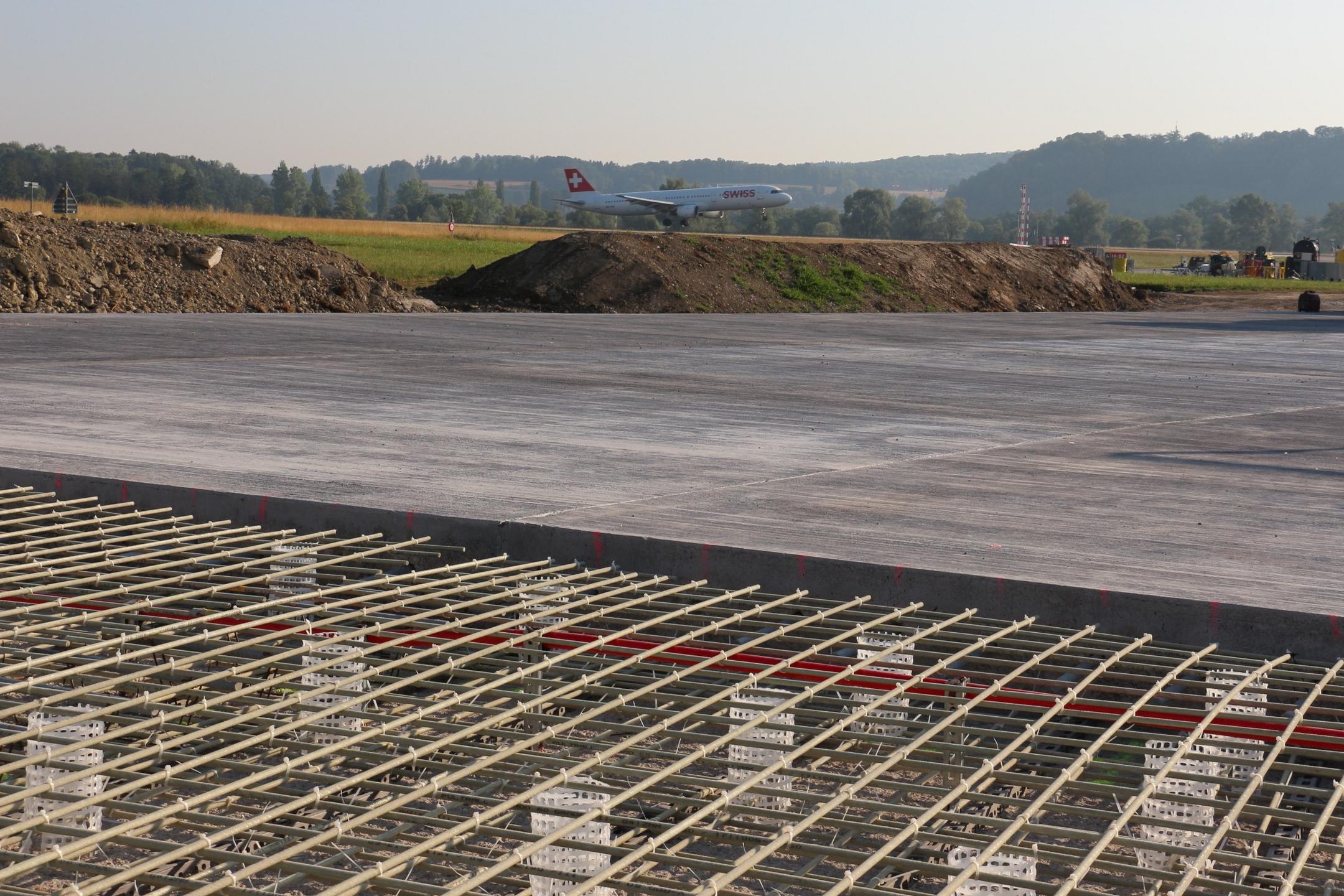 Blick auf die Baustelle aus einer anderen Perspektive, auch hier im Hintergrund grüne Felder und Wälder sowie blauer Himmel.