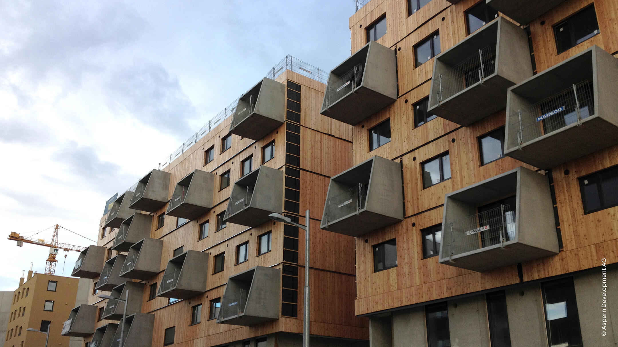 Holzverkleidetes Gebäude mit herausragenden Balkonen vor blauem, leicht bewölktem Himmel