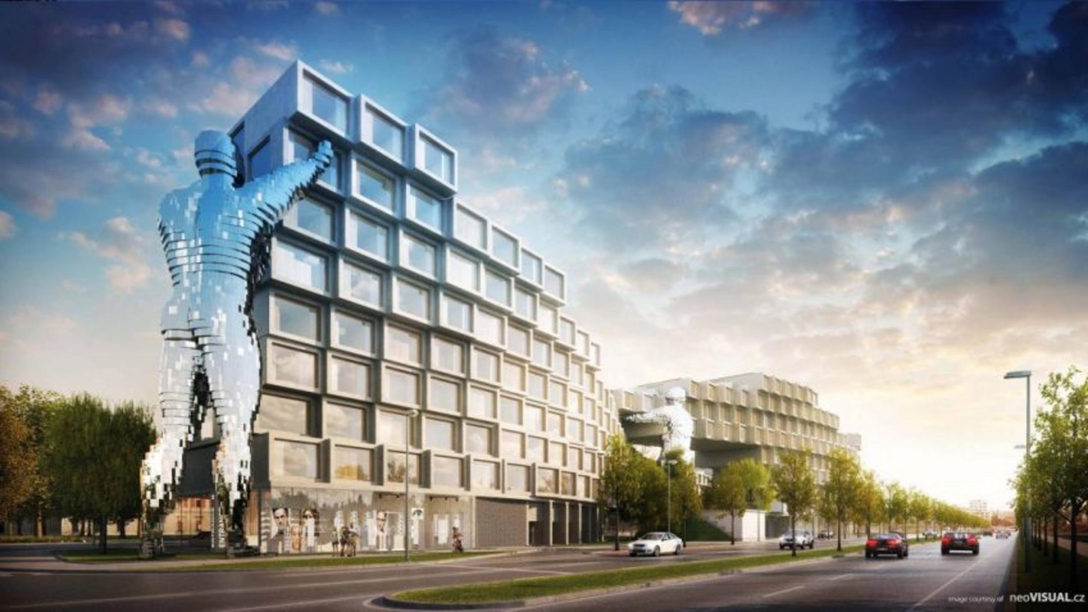 Der stufenartige, moderne Gebäudekomplex vor blauem Himmel aus einer anderen Perspektive, im Vordergrund Grünflächen, eine Straße und Bäume.