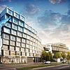 Der stufenartige, moderne Gebäudekomplex vor blauem Himmel aus einer anderen Perspektive, im Vordergrund Grünflächen, eine Straße und Bäume.