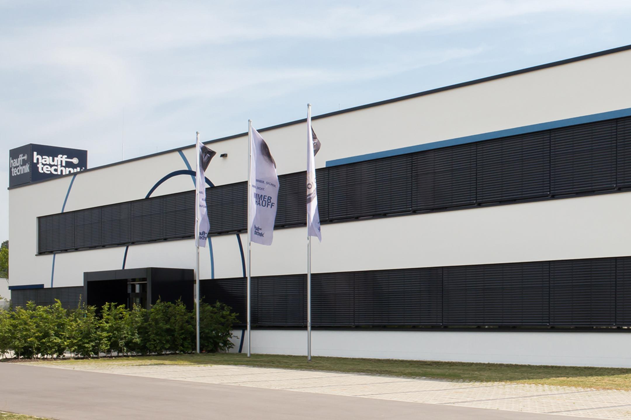 Der Firmenneubau aus mittlerer Entfernung betrachtet, die Fenster schwarz, das Gebäude weiß.