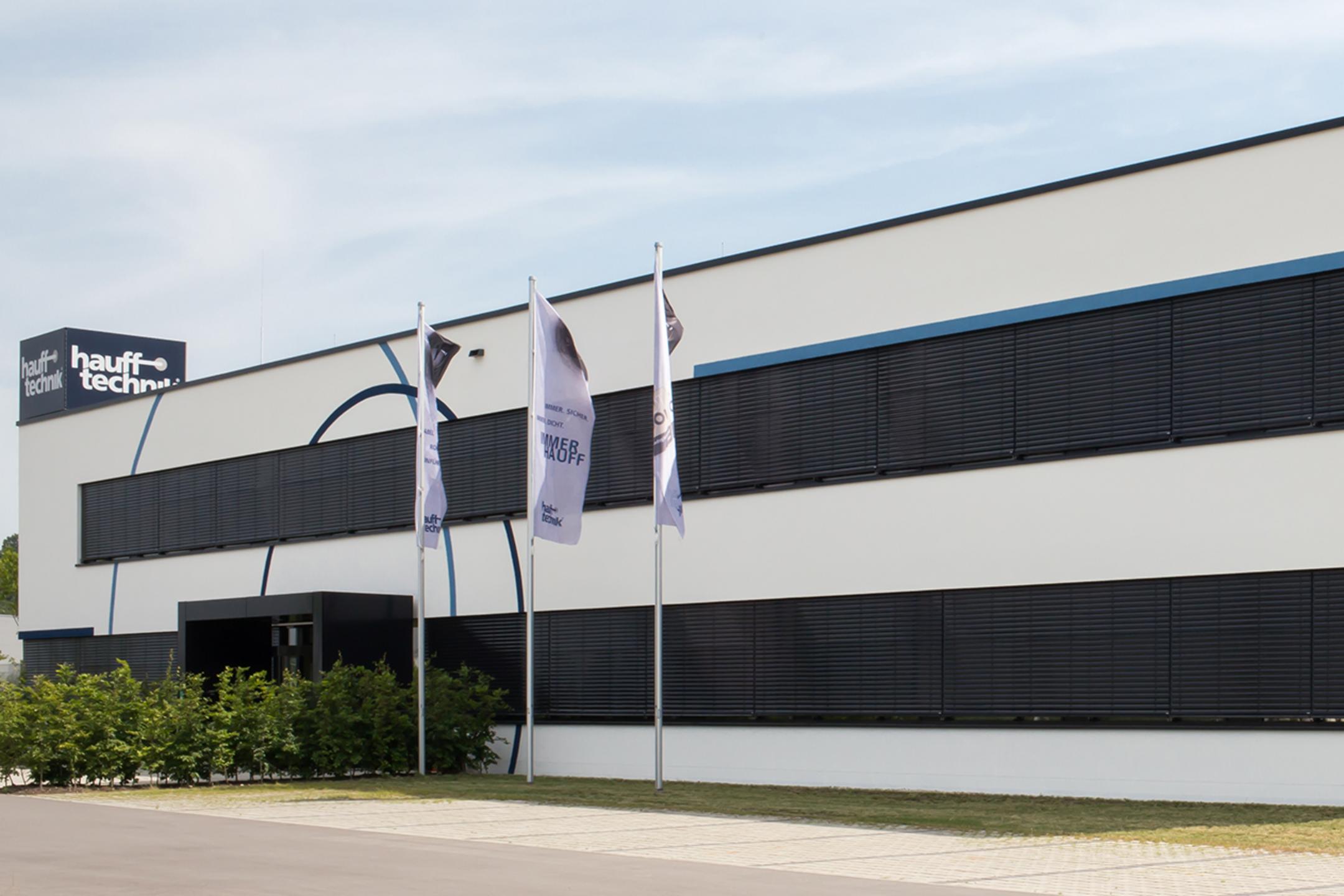 Der Firmenneubau aus mittlerer Entfernung betrachtet, die Fenster schwarz, das Gebäude weiß.