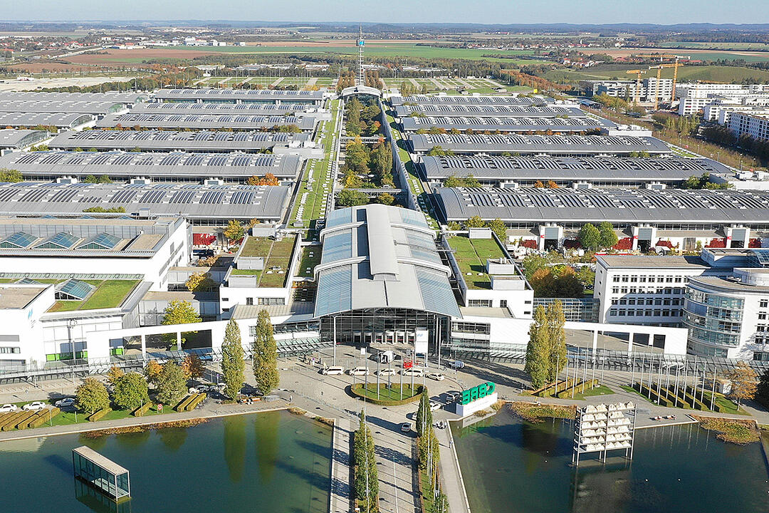 Luftaufnahme der Messe München mit weitläufigen Messehallen und dem Haupteingang im Vordergrund.