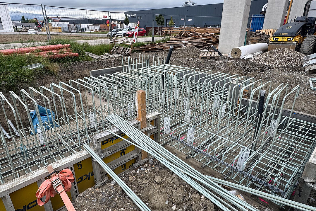 Baustelle mit gerader und gebogener GFK-Bewehrung, Betonstützen und Gebäude im Hintergrund.