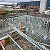 Baustelle mit gerader und gebogener GFK-Bewehrung, Betonstützen und Gebäude im Hintergrund.