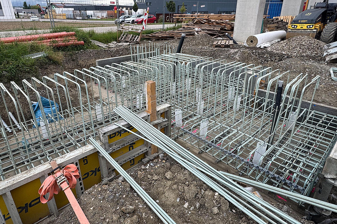 Baustelle mit gerader und gebogener GFK-Bewehrung, Betonstützen und Gebäude im Hintergrund.