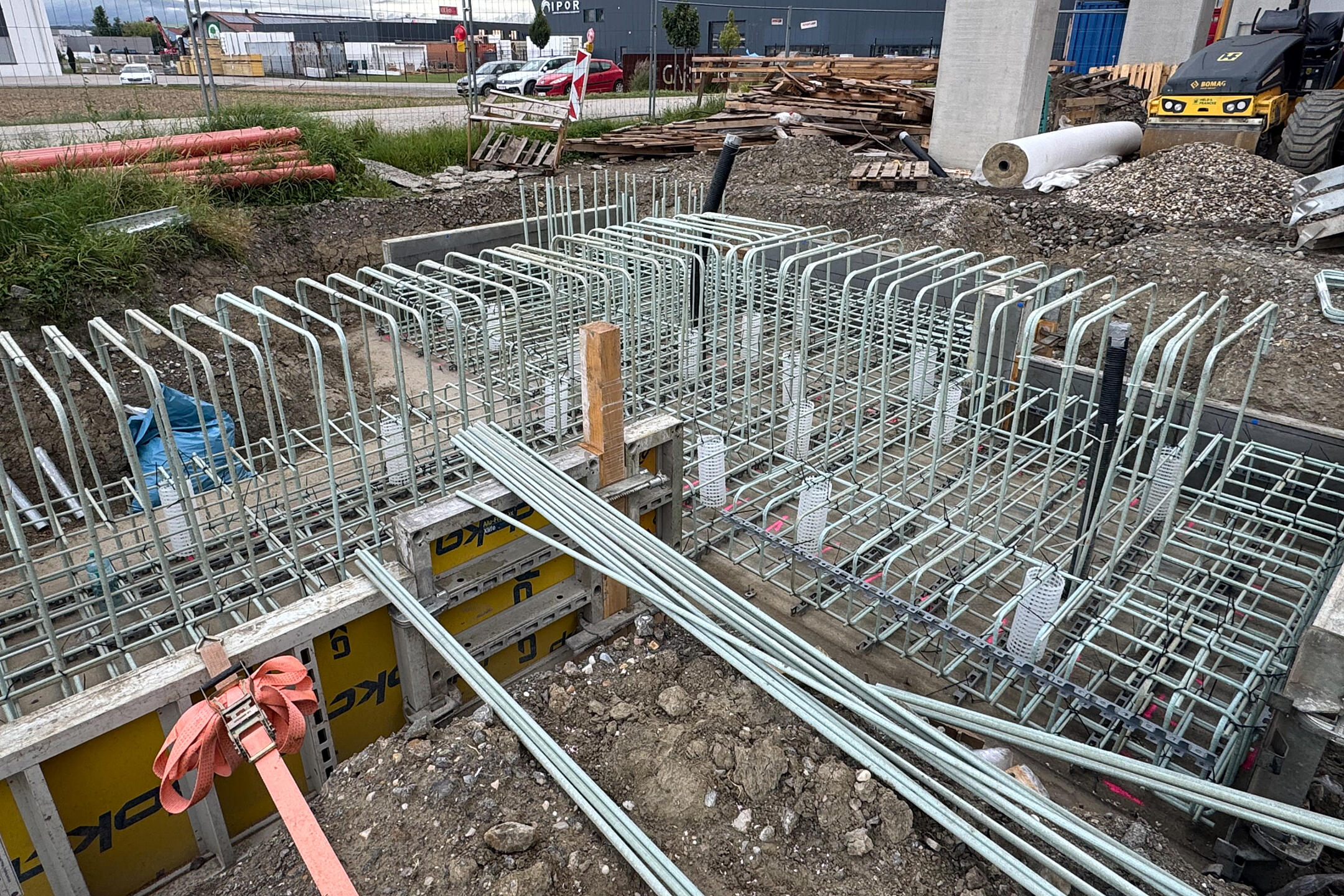 Baustelle mit gerader und gebogener GFK-Bewehrung, Betonstützen und Gebäude im Hintergrund.