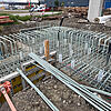 Baustelle mit gerader und gebogener GFK-Bewehrung, Betonstützen und Gebäude im Hintergrund.