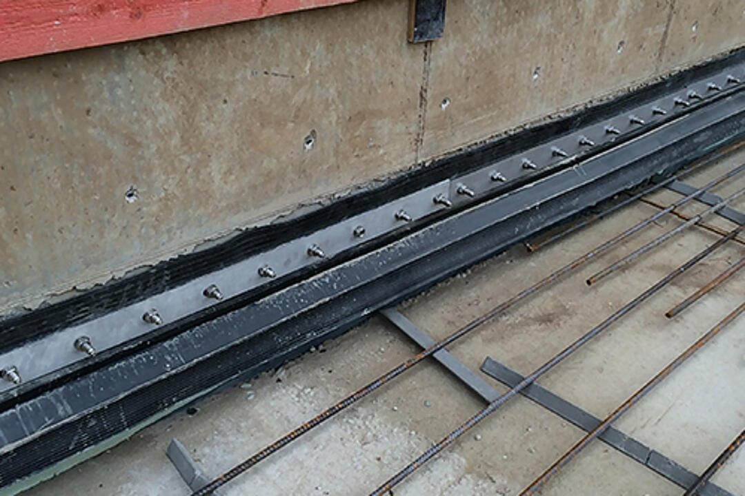 Nahaufnahme einer Baustelle mit Abdichtungselementen, Bewehrungsgitter und roten Holzplanken