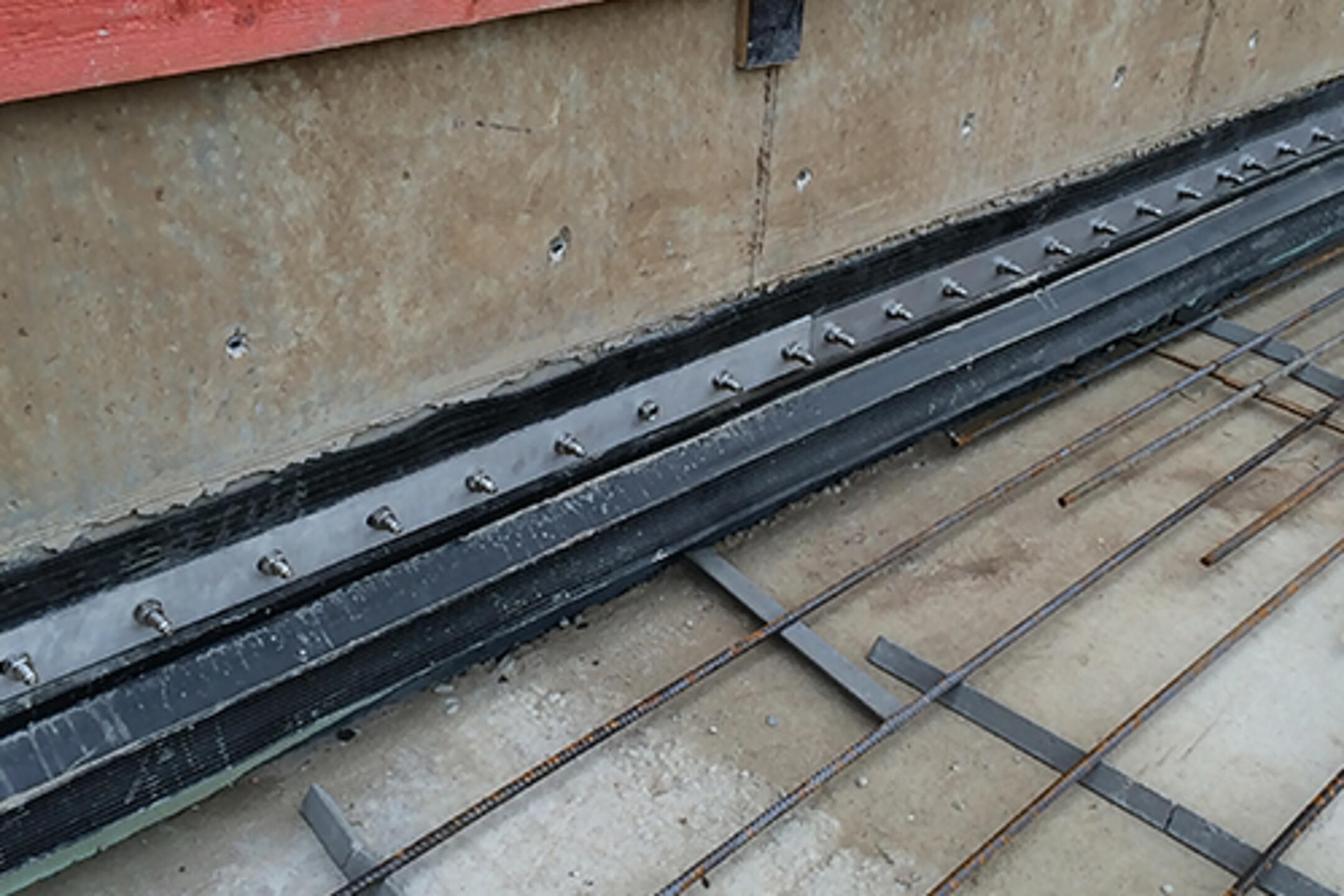 Nahaufnahme einer Baustelle mit Abdichtungselementen, Bewehrungsgitter und roten Holzplanken