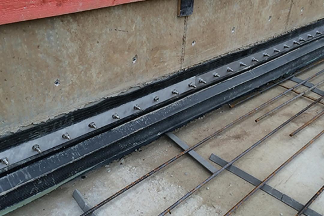 Nahaufnahme einer Baustelle mit Abdichtungselementen, Bewehrungsgitter und roten Holzplanken