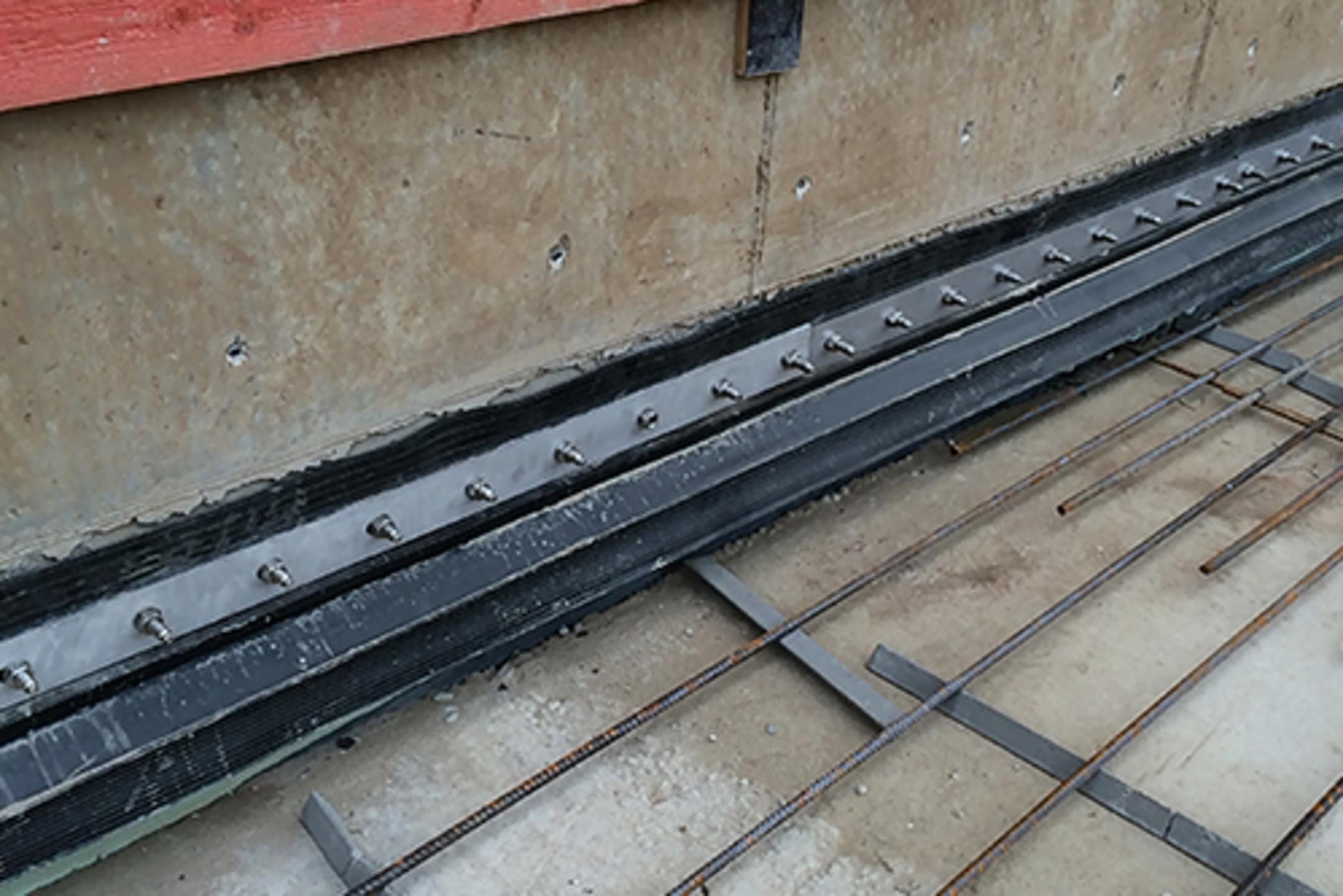 Nahaufnahme einer Baustelle mit Abdichtungselementen, Bewehrungsgitter und roten Holzplanken