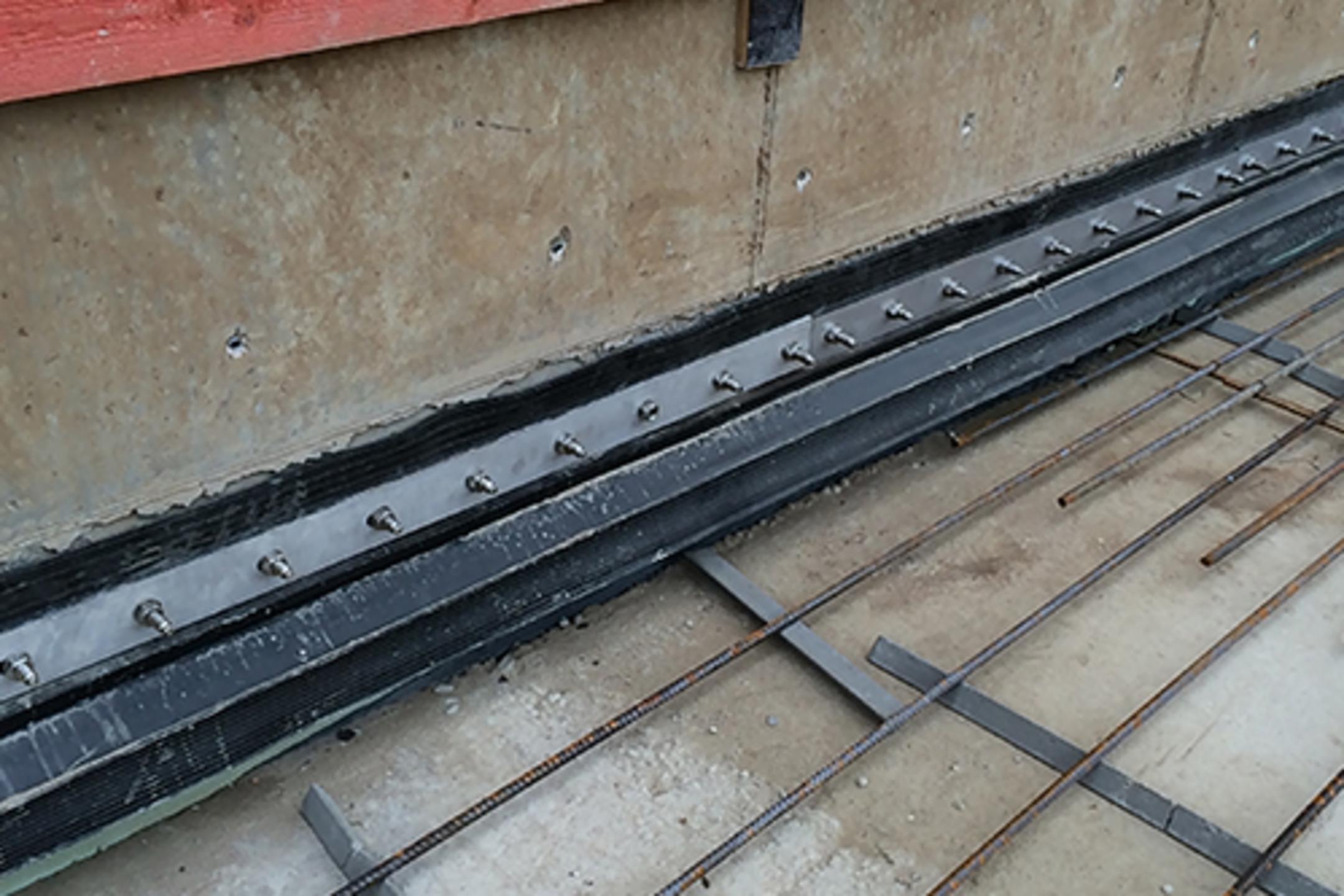 Nahaufnahme einer Baustelle mit Abdichtungselementen, Bewehrungsgitter und roten Holzplanken