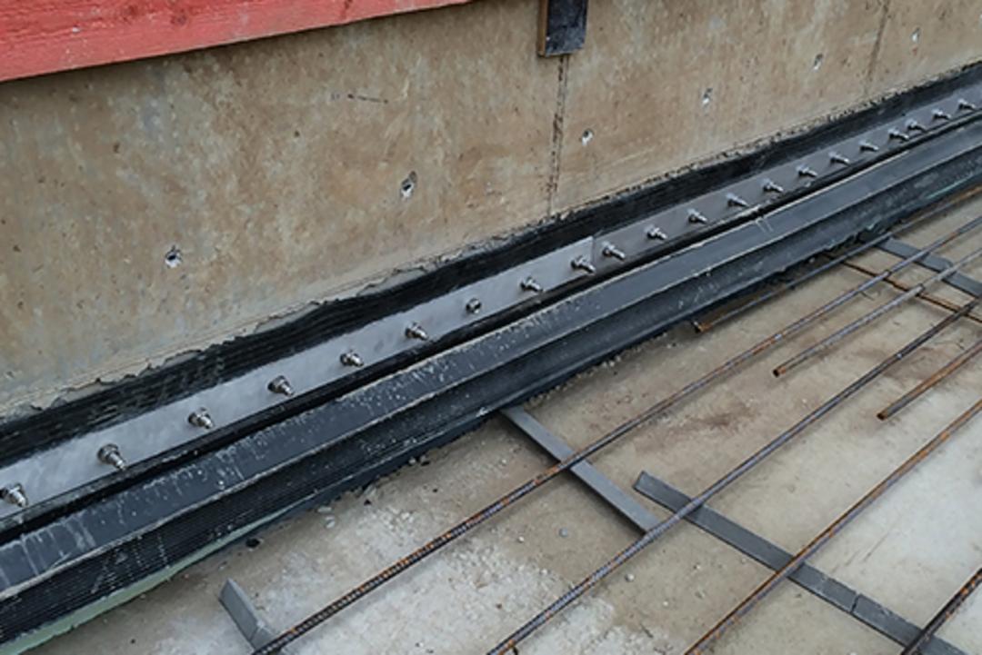 Nahaufnahme einer Baustelle mit Abdichtungselementen, Bewehrungsgitter und roten Holzplanken