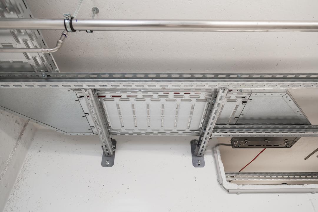 Installierte Kabeltrassen und Rohrleitungen an einer Betondecke, sichtbar in einem Technik- oder Versorgungsraum