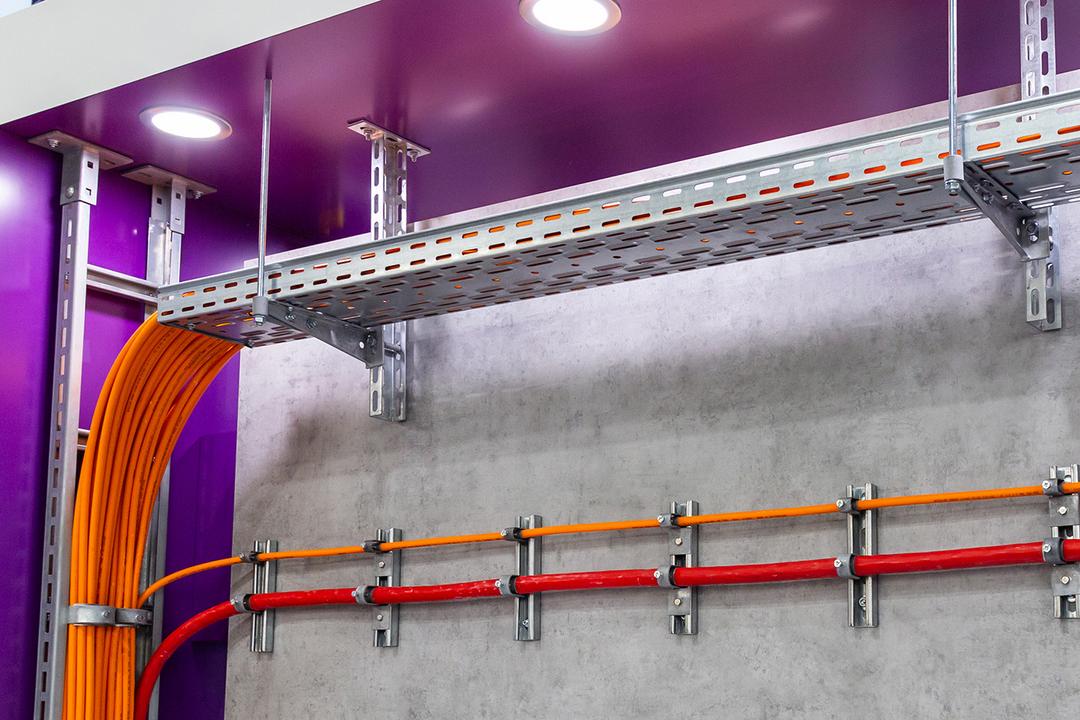 Kabelrinne unter der Decke mit orangefarbenen Kabeln sowie Wandmontage von Leitungen an Montageschienen.
