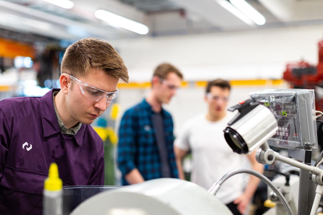 Mitarbeiter in einer Produktion mit Schutzbrille und lilafarbenem Overall mit PohlCon-Logo