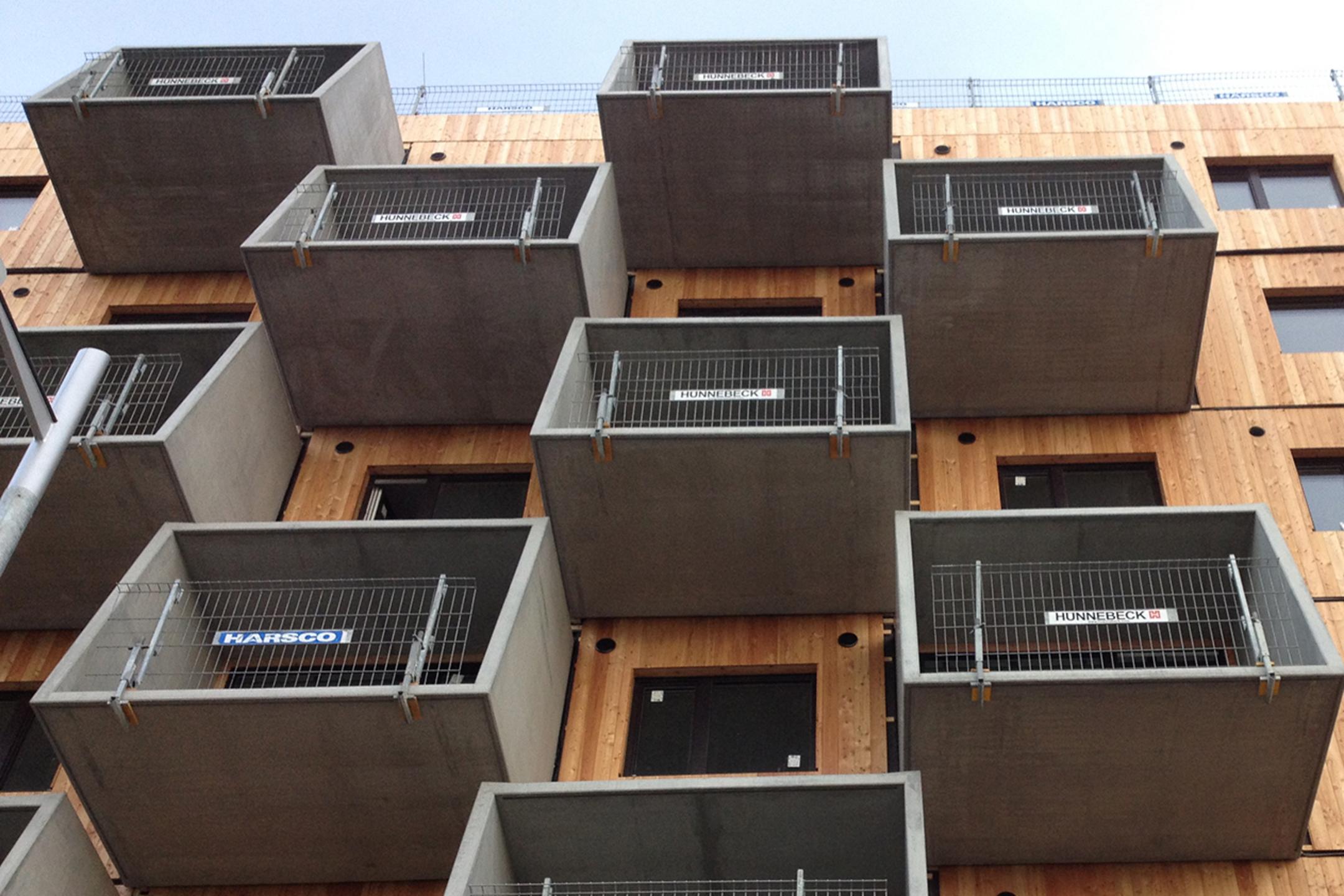 Blick von unten auf die Holzfassade mit den Betonbalkonen und provisorischen Geländern